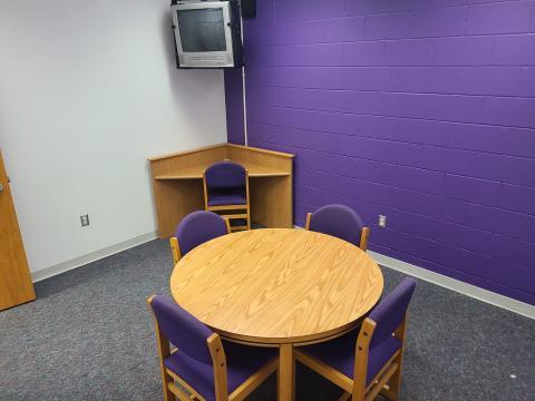 Riverside study room A24 with table, four padded chairs, corner desk with chair, and ceiling mounted CRT television with DVD player.