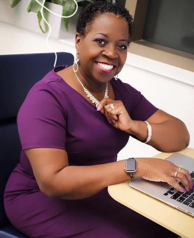 Author Renee Ecckles-Hardy seated wearing purple dress with a book