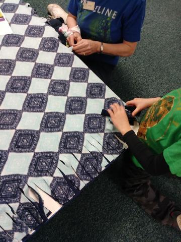 Blue and white fleece blanket with hands tying knots 