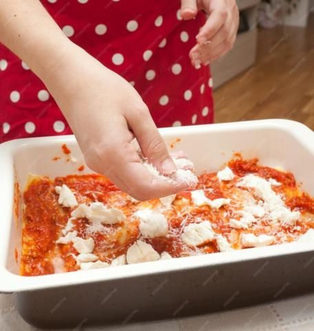 Child's hand adding cheese to dish of homemade lasagna